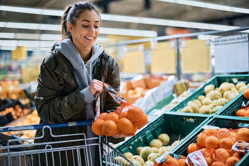 Happy woman buying oranges in plastic mesh at supermarket.