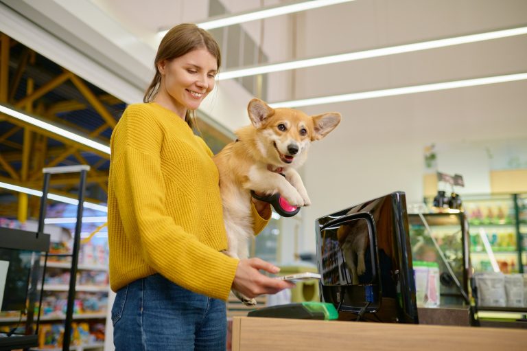 Young satisfied woman paying for purchase at pet shop counter desk